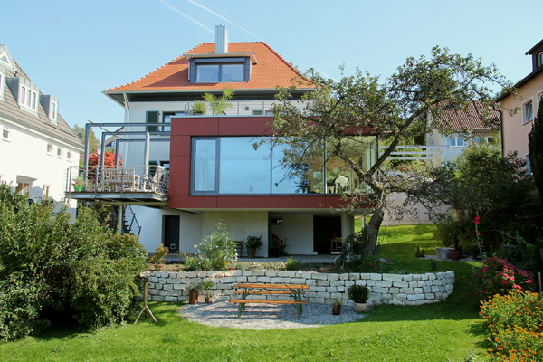Umgebautes Wohnhaus mit rot gerahmtem Glasanbau und Garten